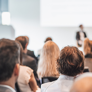 Publikum blickt auf eine Bühne während einer Tagung, Rückansicht mehrerer Konferenzteilnehmender.